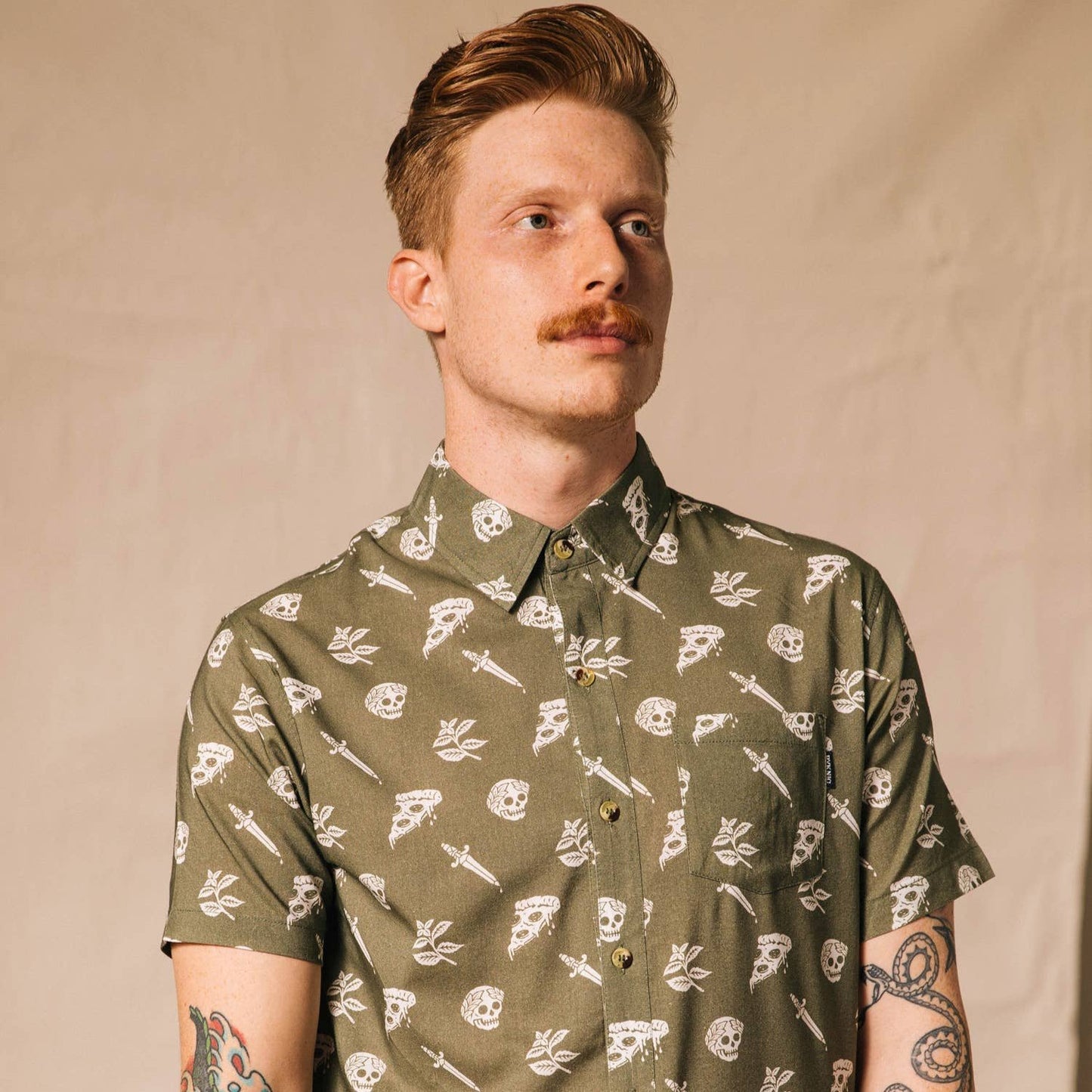 Man wearing a button up shirt that is oregano green with skulls, pizza and swords on it.