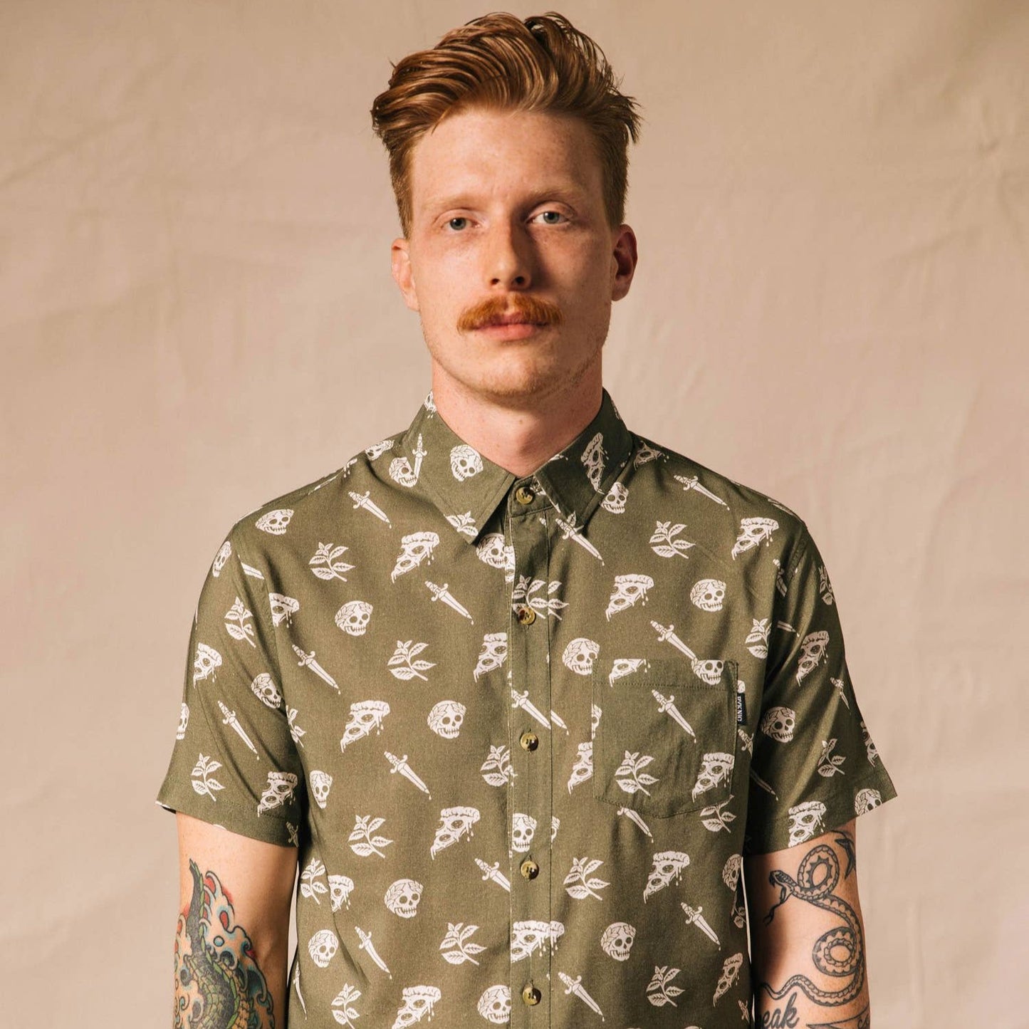 Man wearing a button up shirt that is oregano green with skulls, pizza and swords on it.