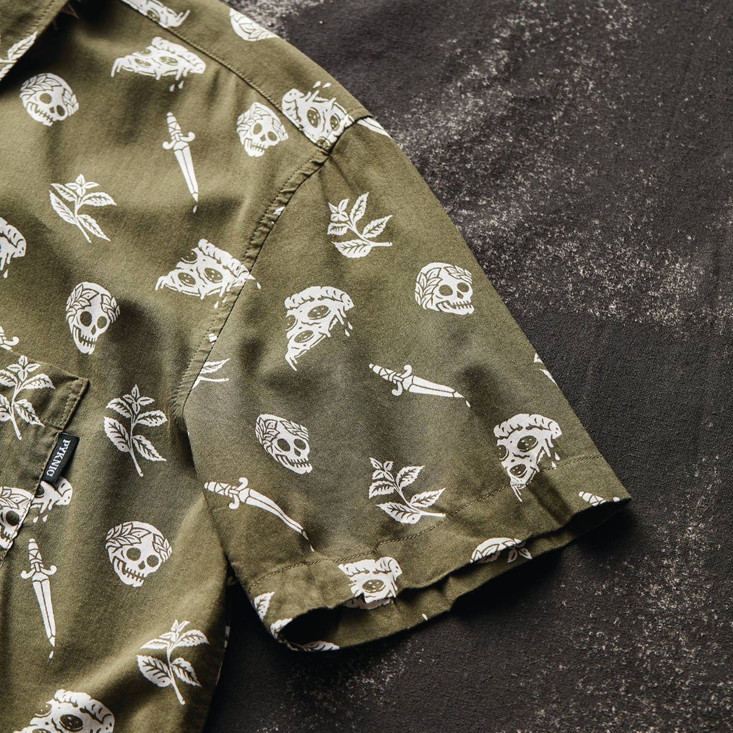 button up shirt that is oregano green with skulls, pizza and swords on it.