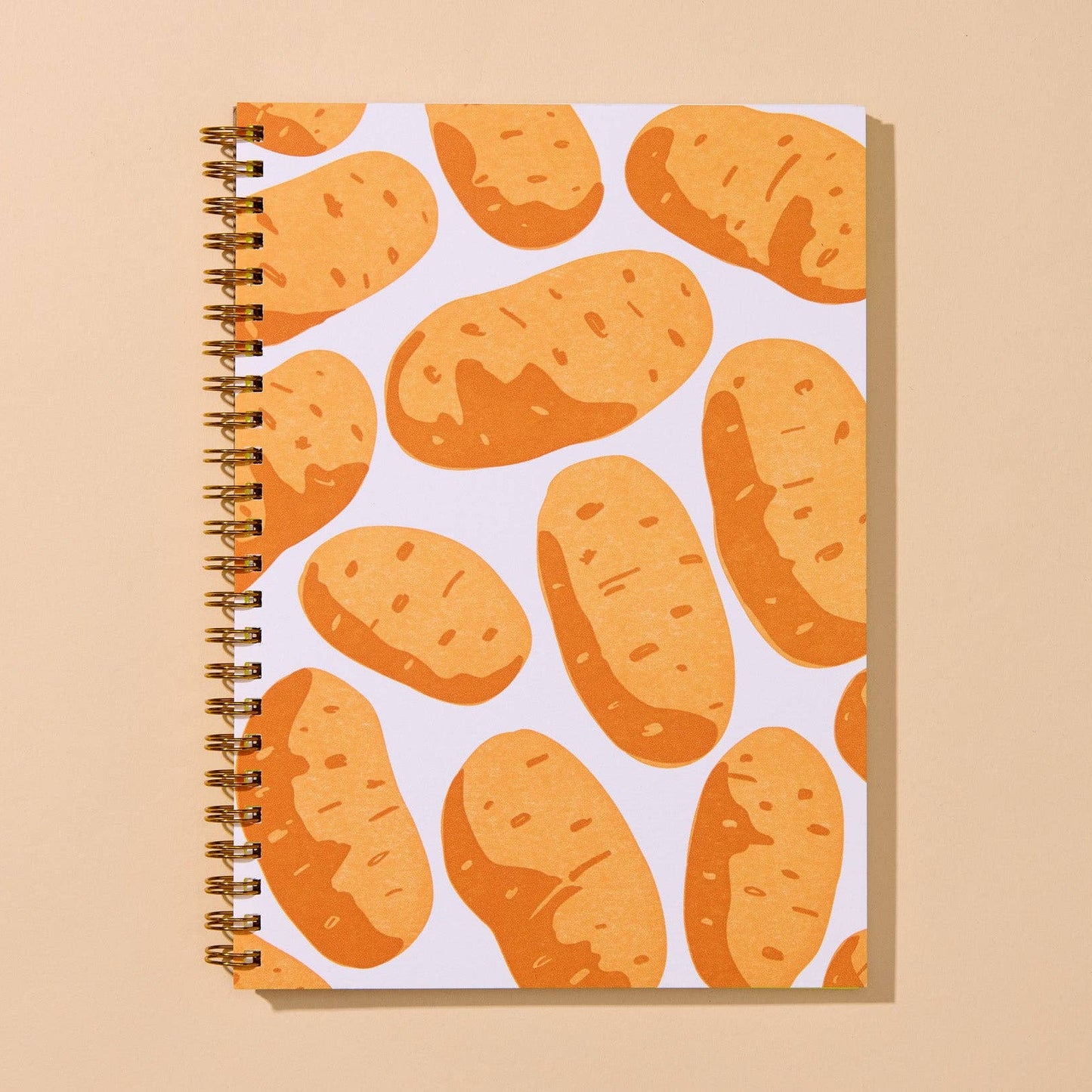 A spiral-bound notebook with a white cover decorated with a repeating pattern of illustrated orange-brown potatoes, set against a solid beige background.