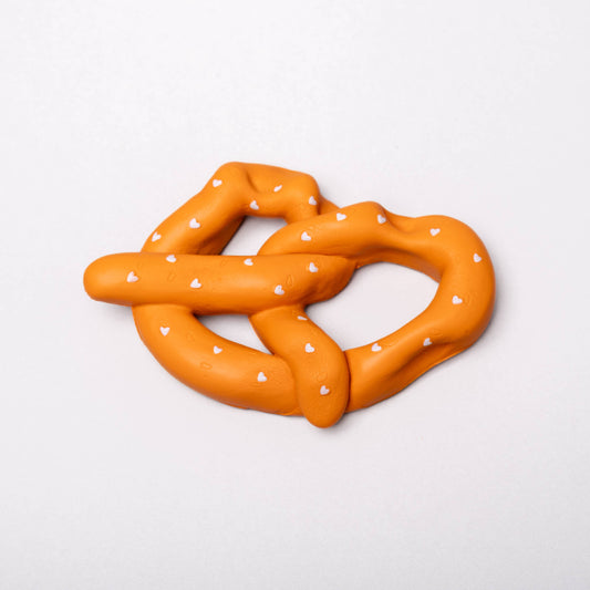 Orange pretzel-shaped toy with white polka dots on a white background