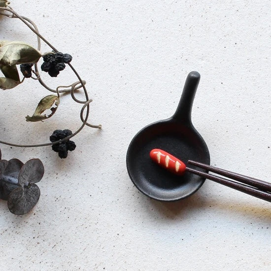 Mini chopstick holder that looks like a cast iron pan with a sausage inside.