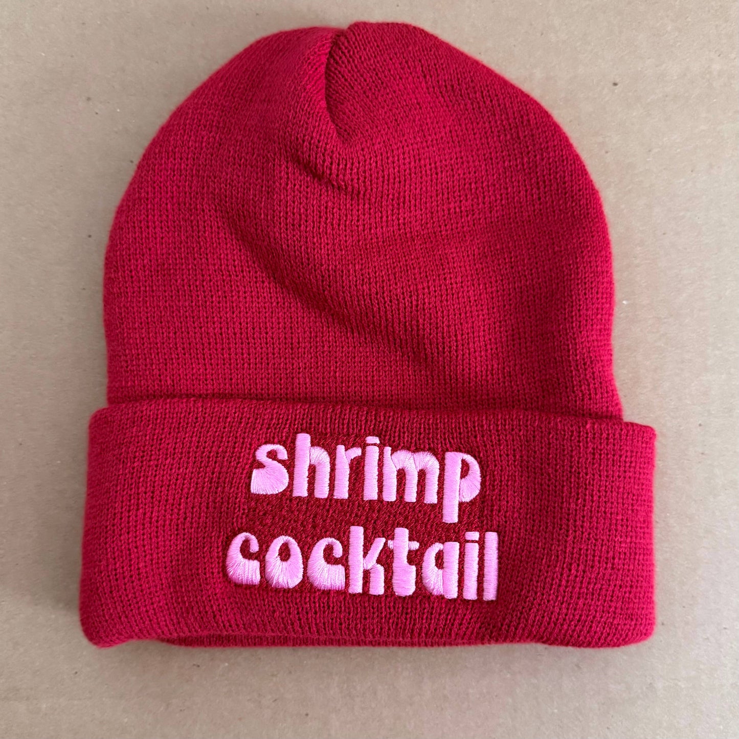Red beanie with 'shrimp cocktail' text on a beige background