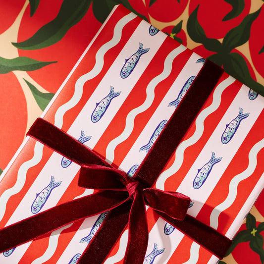 Gift wrapped in red and white striped paper with blue fish patterns, tied with a red ribbon, against a red background with green leaves.