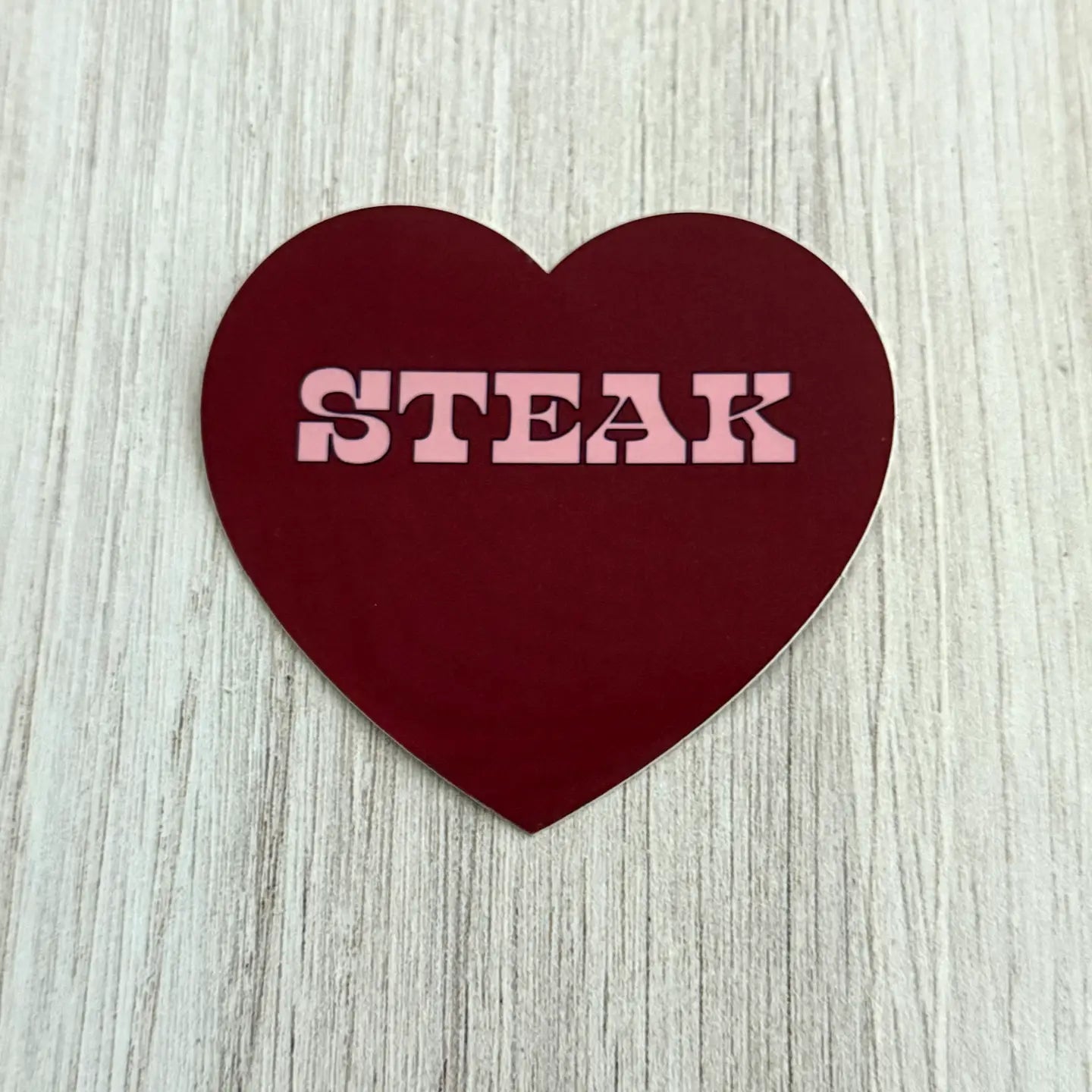 Heart-shaped sign with 'STEAK' text on a wooden surface