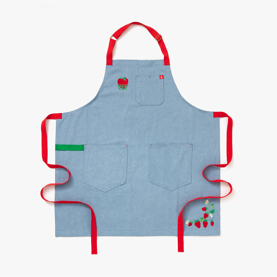 Blue apron with red straps. This apron is dedicated to strawberries with embroidery of strawberries in a basket and on a vine with little white flowers.