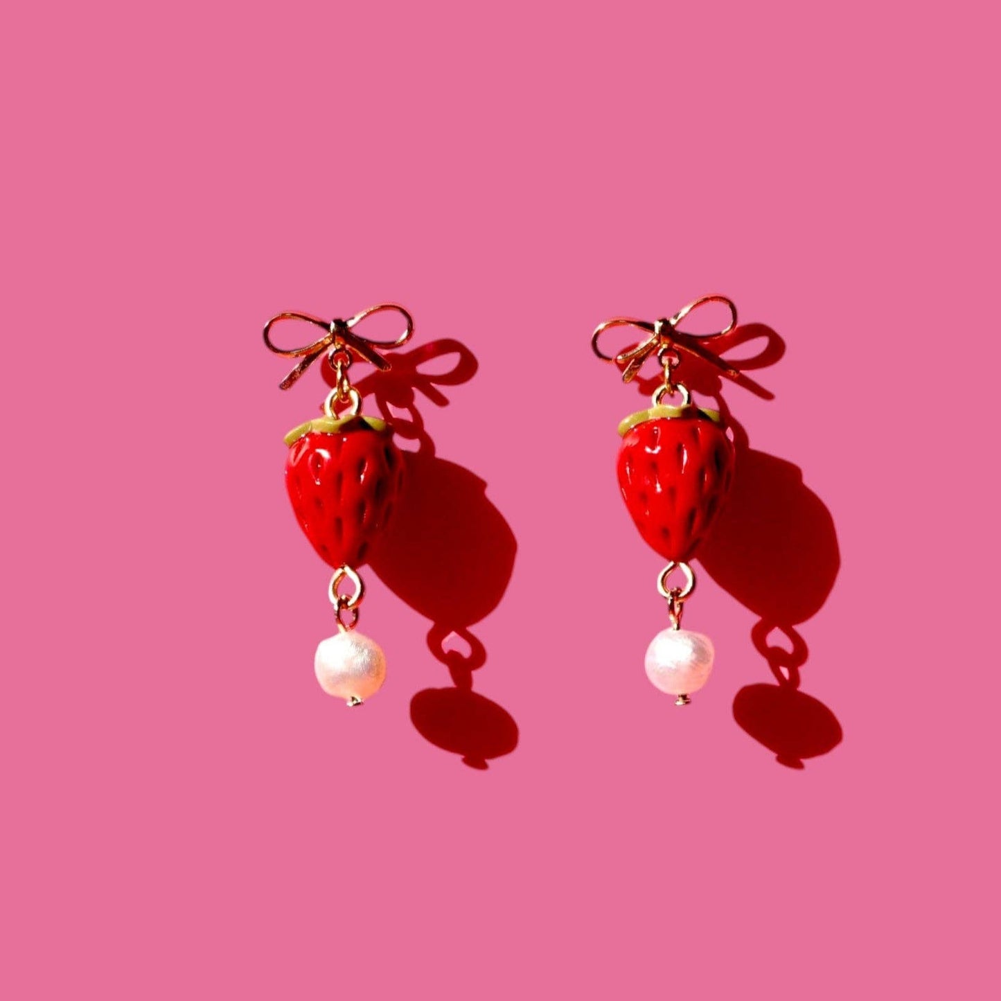 Strawberry-shaped earrings with pearl drops on a pink background