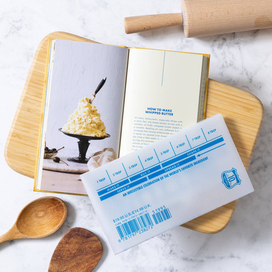 Parchment sleeve for The Butter Book with measurement markings next to a cookbook on a marble surface