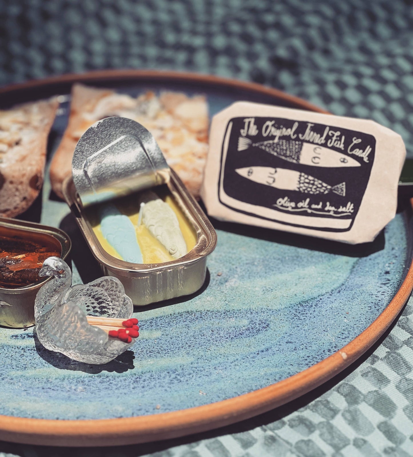 Opened tinned fish candle with outer paper packaging next to it