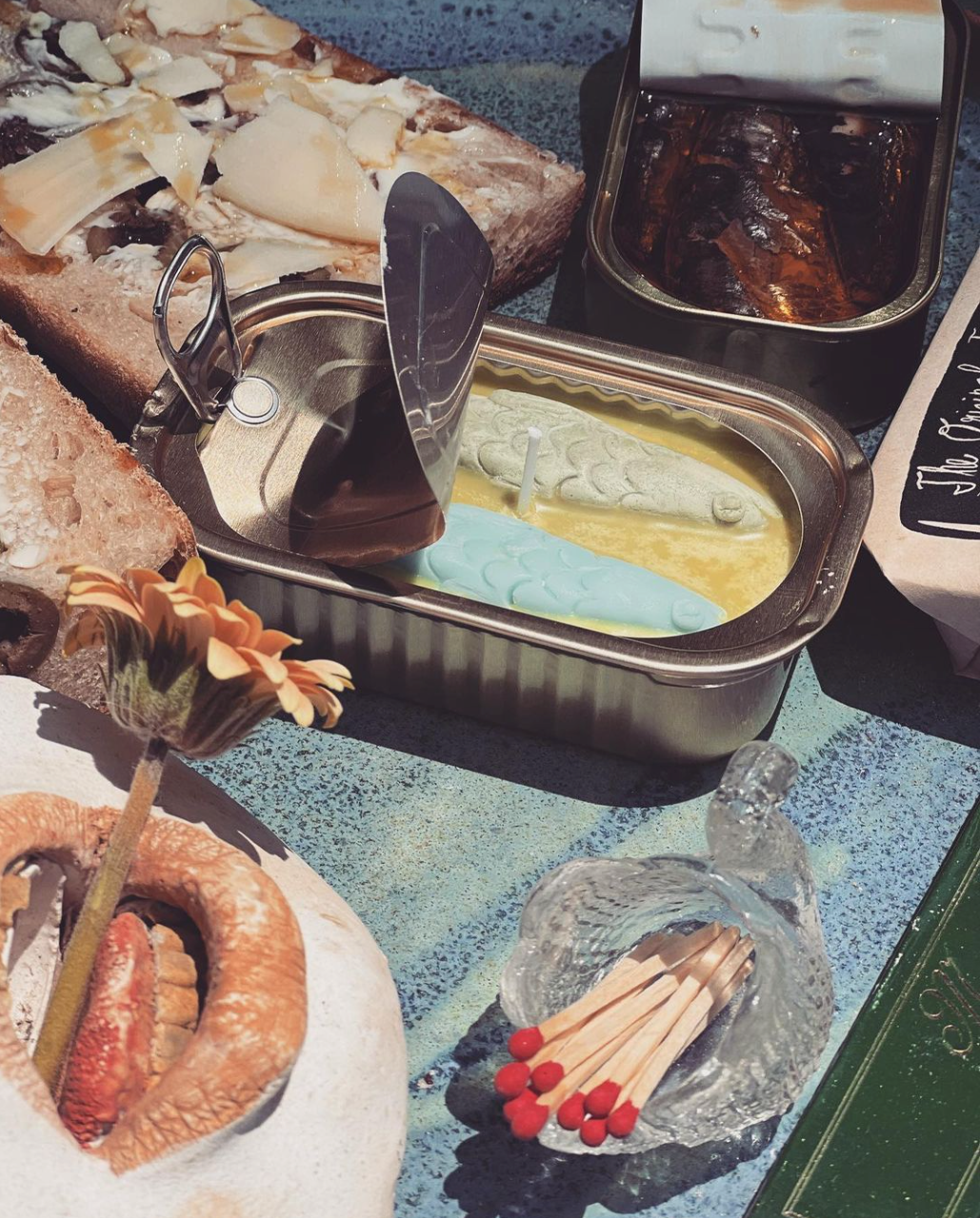 Opened tinned fish candle next to actual tinned fish