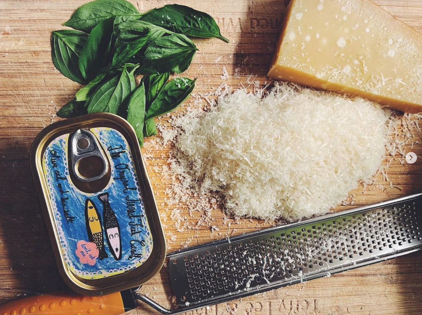 Closed tinned fish candle on a cutting board with basil leaves and grated cheese