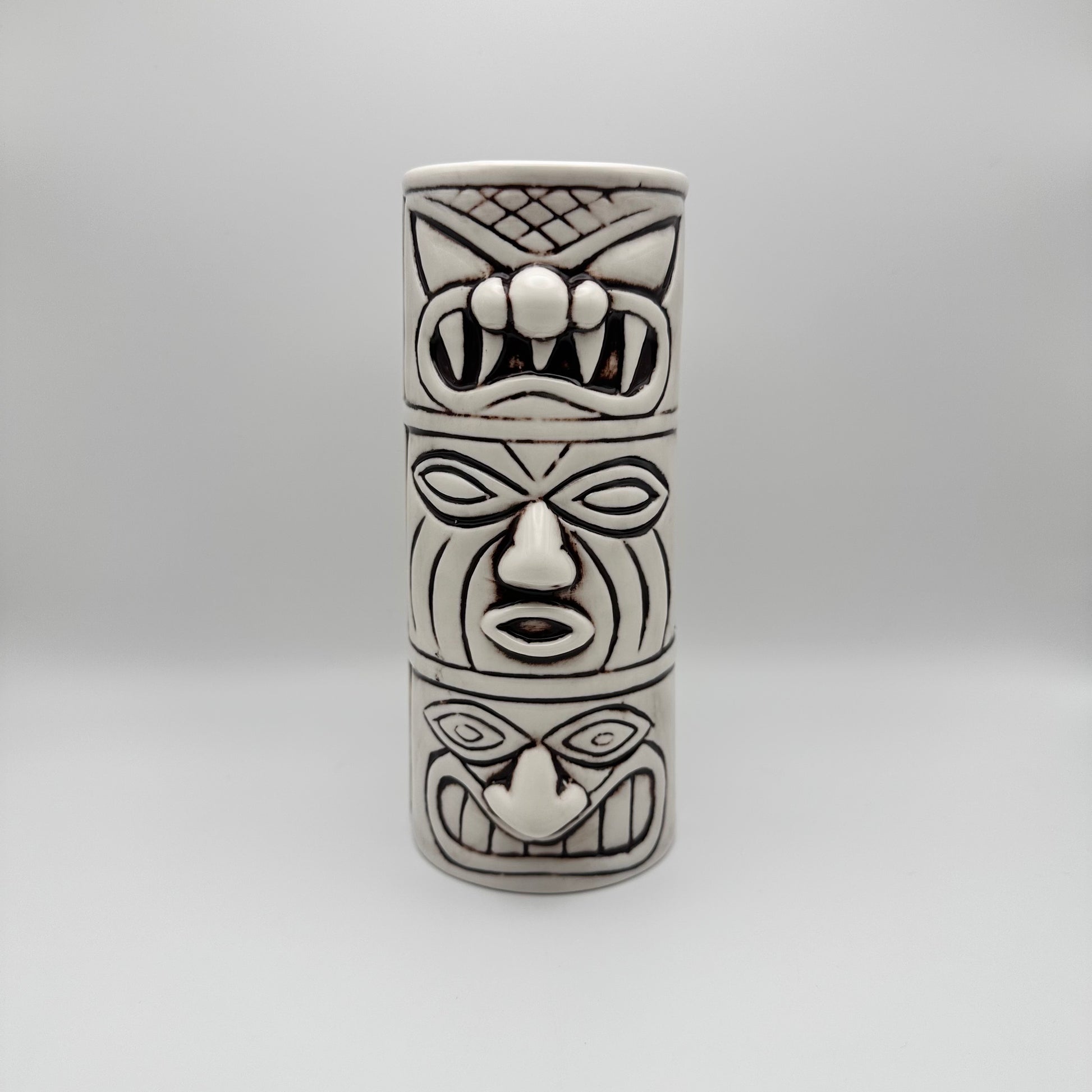Cylindrical ceramic vase with tiki mask design on a white background