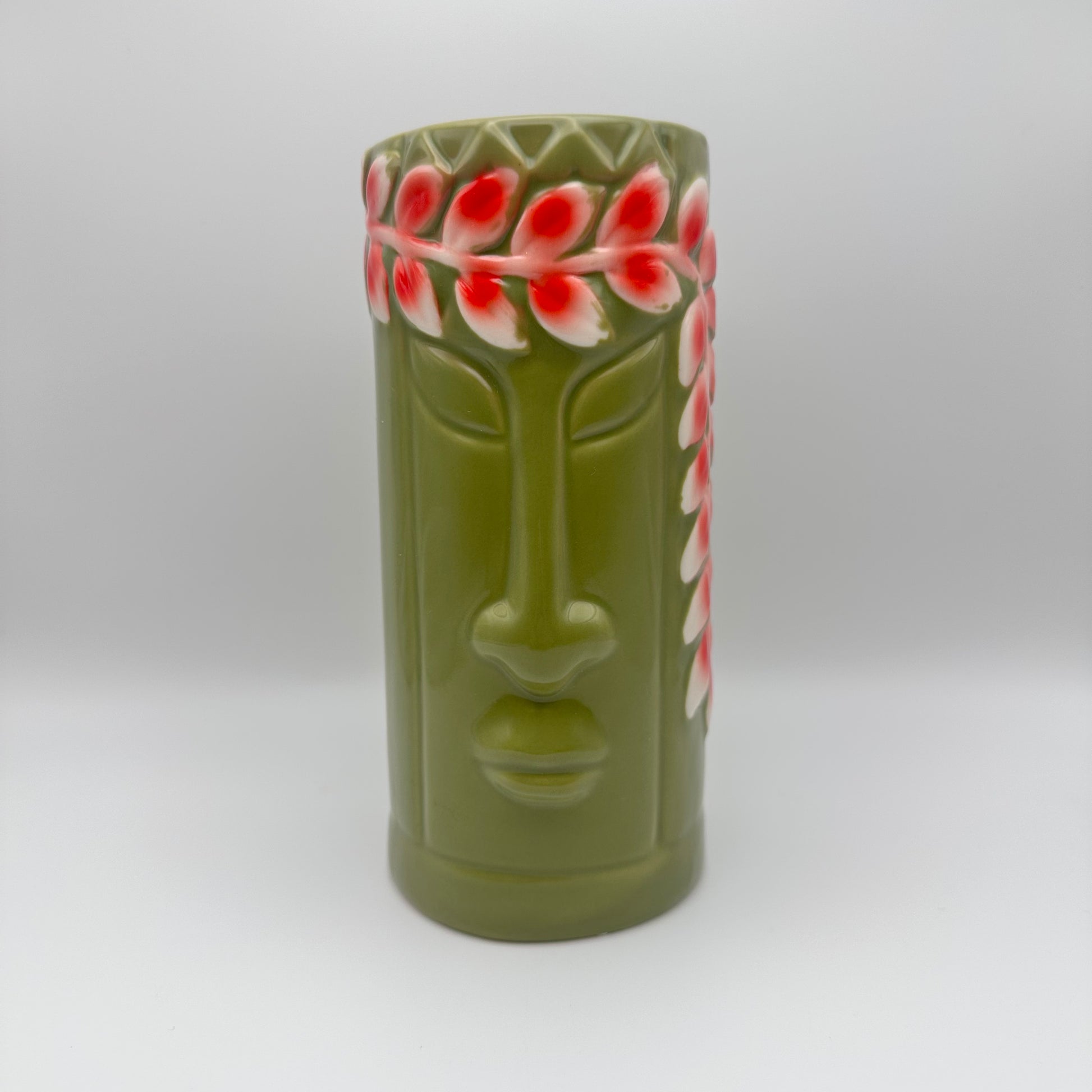 Green ceramic vase with face design and red floral patterns on a white background