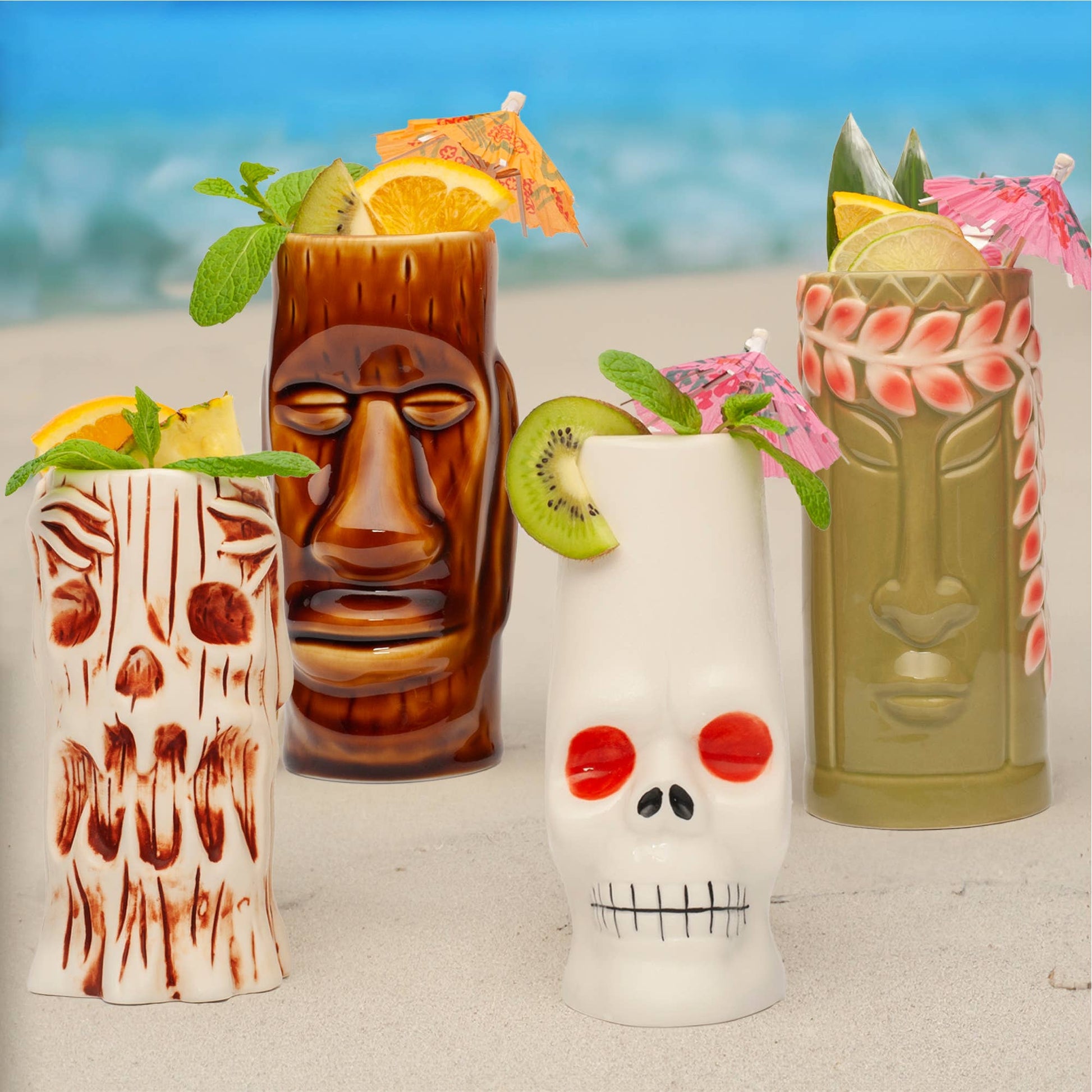 Four tiki-style glasses with tropical drinks and garnishes on a beach setting