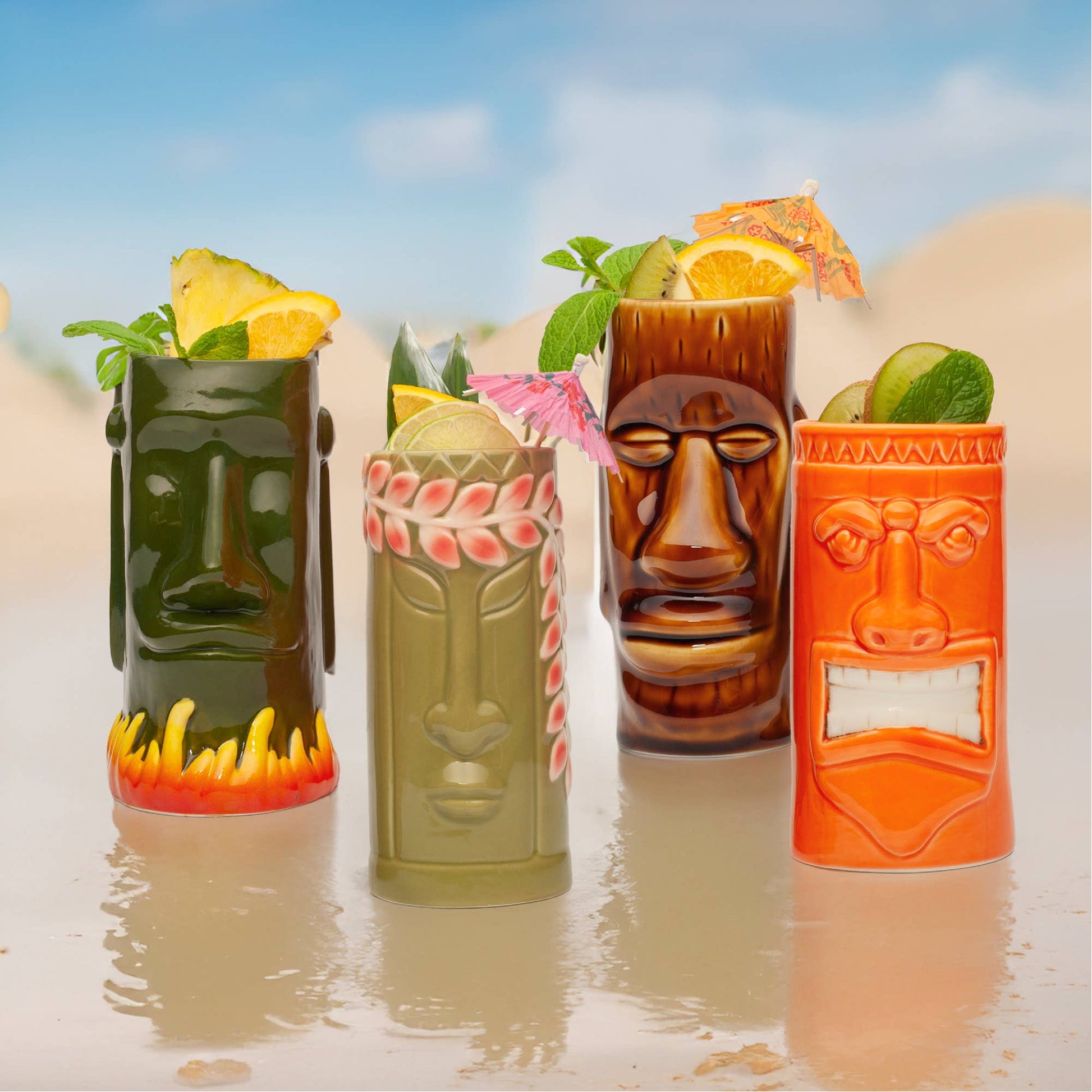 Four tiki mugs with face designs filled with tropical drinks against a beach background.