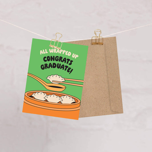Graduation card with dumplings and text 'All wrapped up congrats graduate!' on a string.
