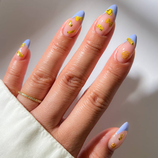 Hand with pastel blue and pink nails with yellow pasta sticker accents on a neutral background