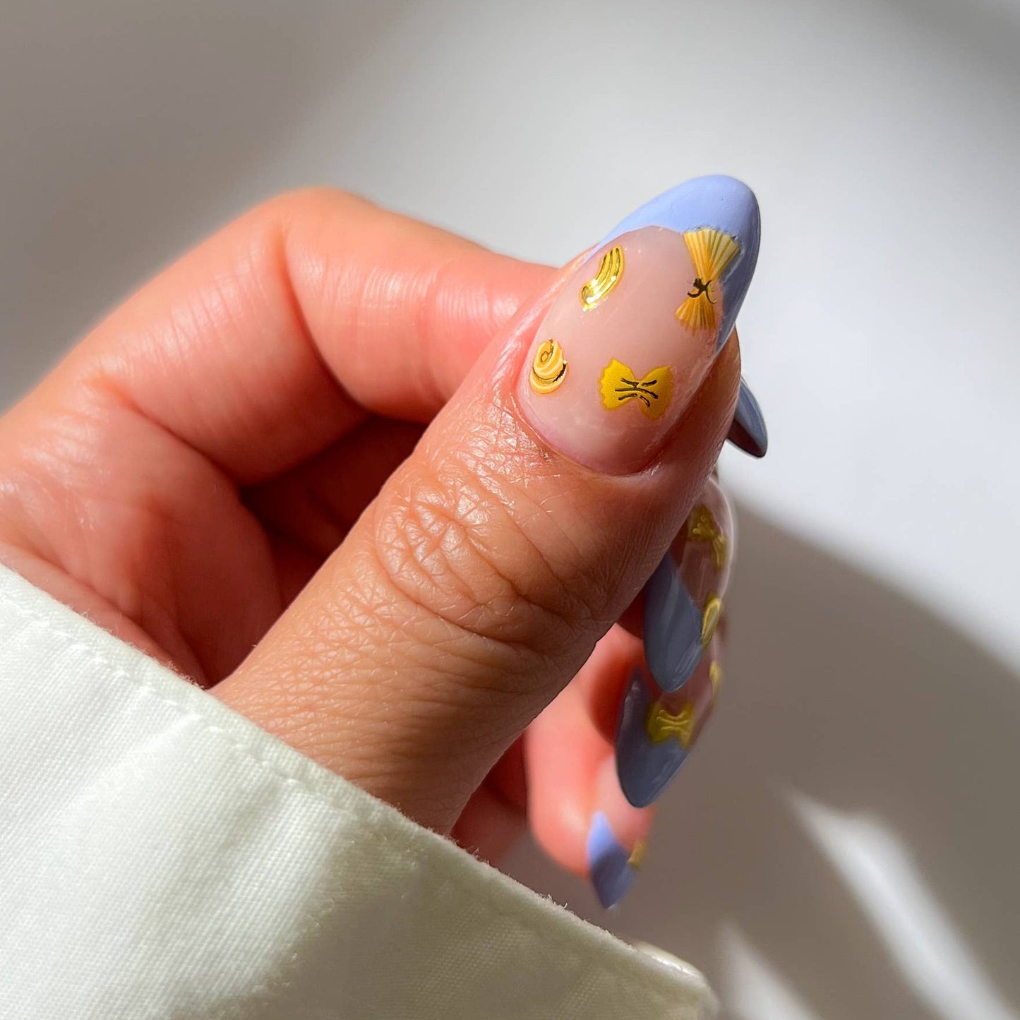 Hand with blue nail polish featuring yellow pasta designs on a neutral background