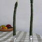 Two green tapered candles that look like stalks of asparagus in silver candle holders 