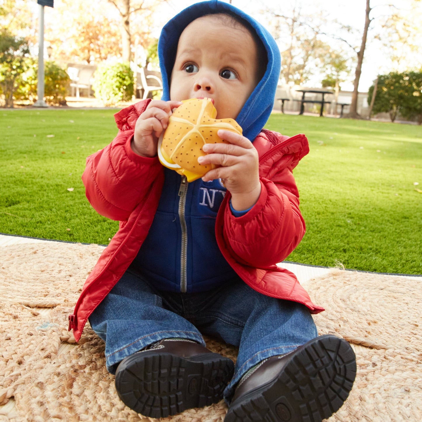 Child in a red and blue jacket eating a sandwich teether outdoors