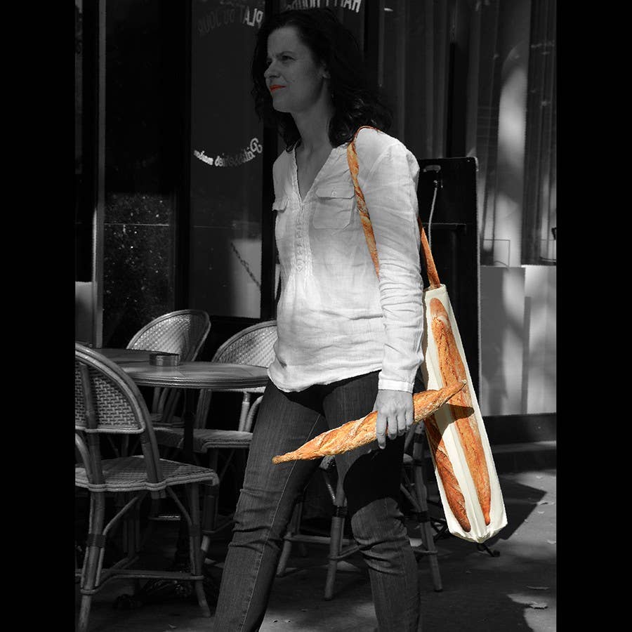 black and white image of lady holding a baguette with her baguette bag on her shoulder.