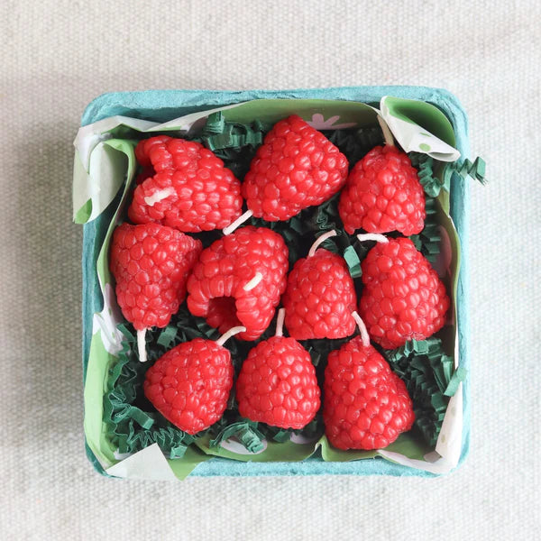 Red raspberry-shaped candles in a box on a light gray background