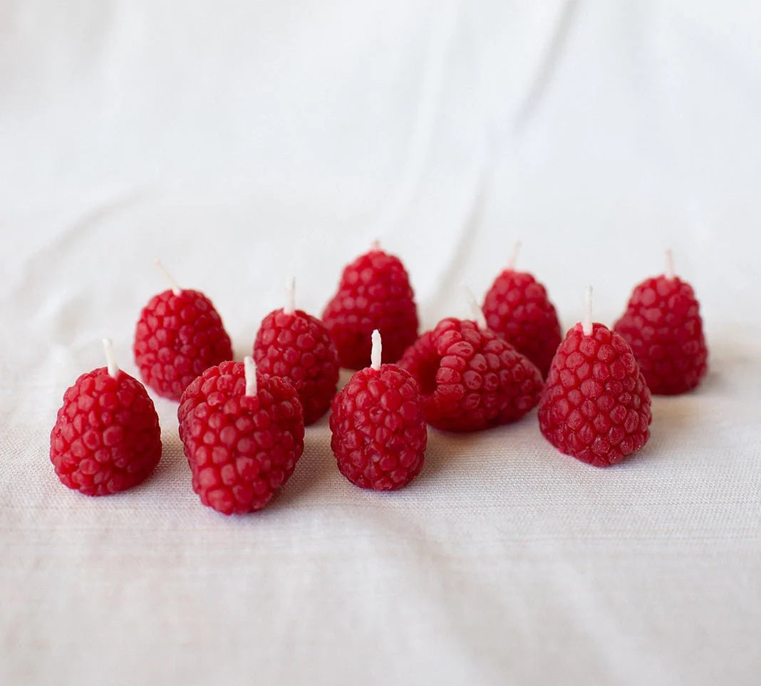 Red raspberry-shaped candles on a white fabric background