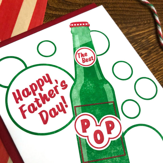Father's Day card with a green bottle design and 'Happy Father's Day!' text on a wooden surface.