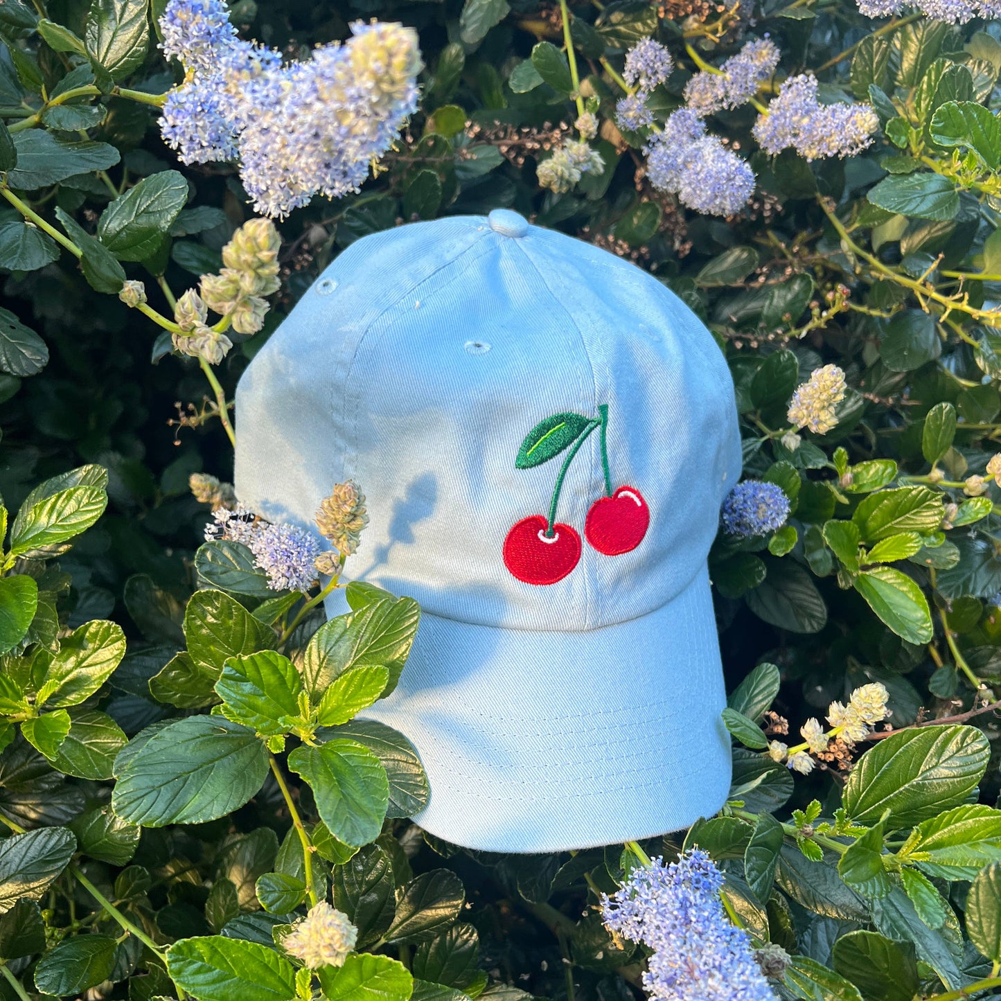 Two red cherries with green stem embroidered on middle front of baby blue hat.