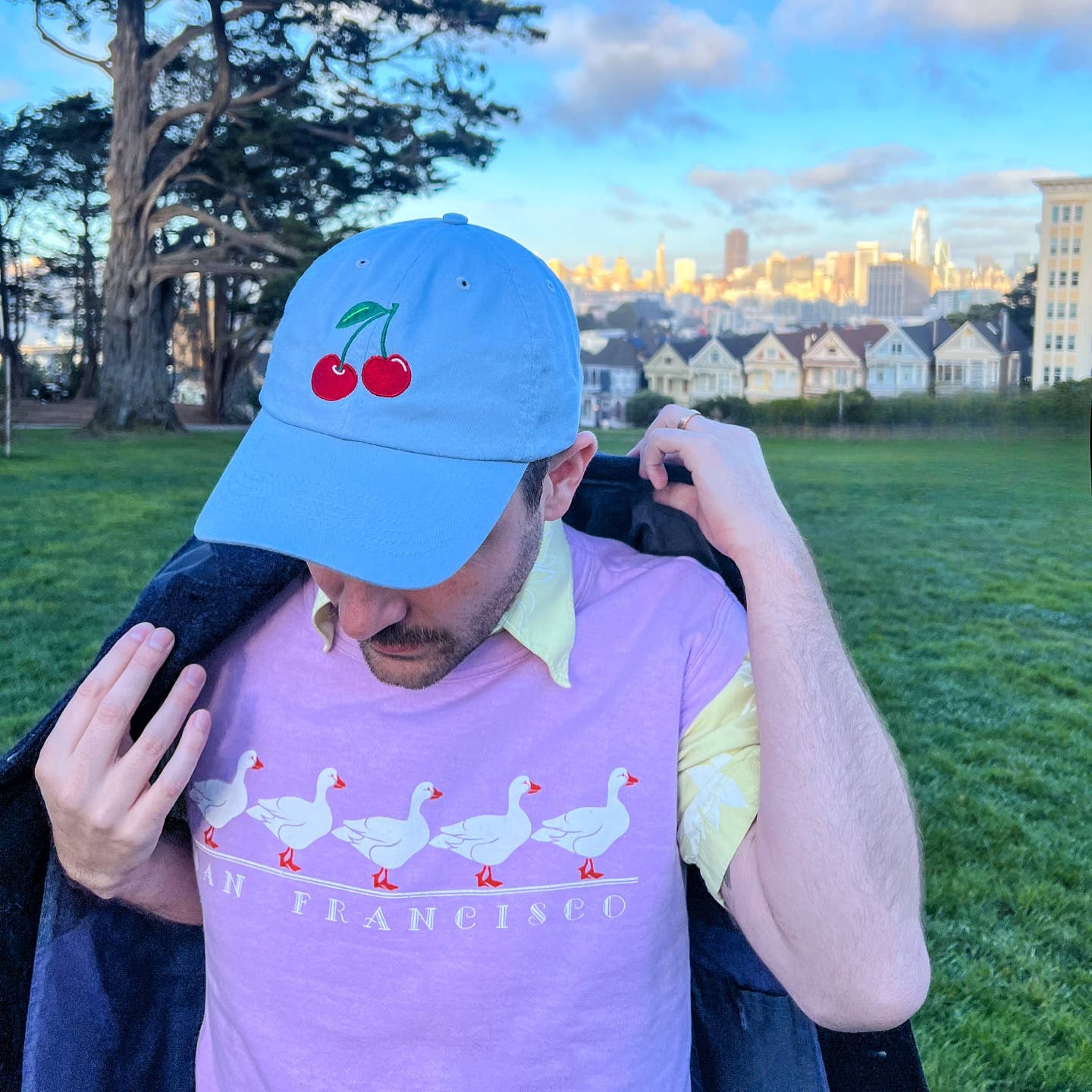 Two red cherries with green stem embroidered on middle front of baby blue hat. Seen here worn on person