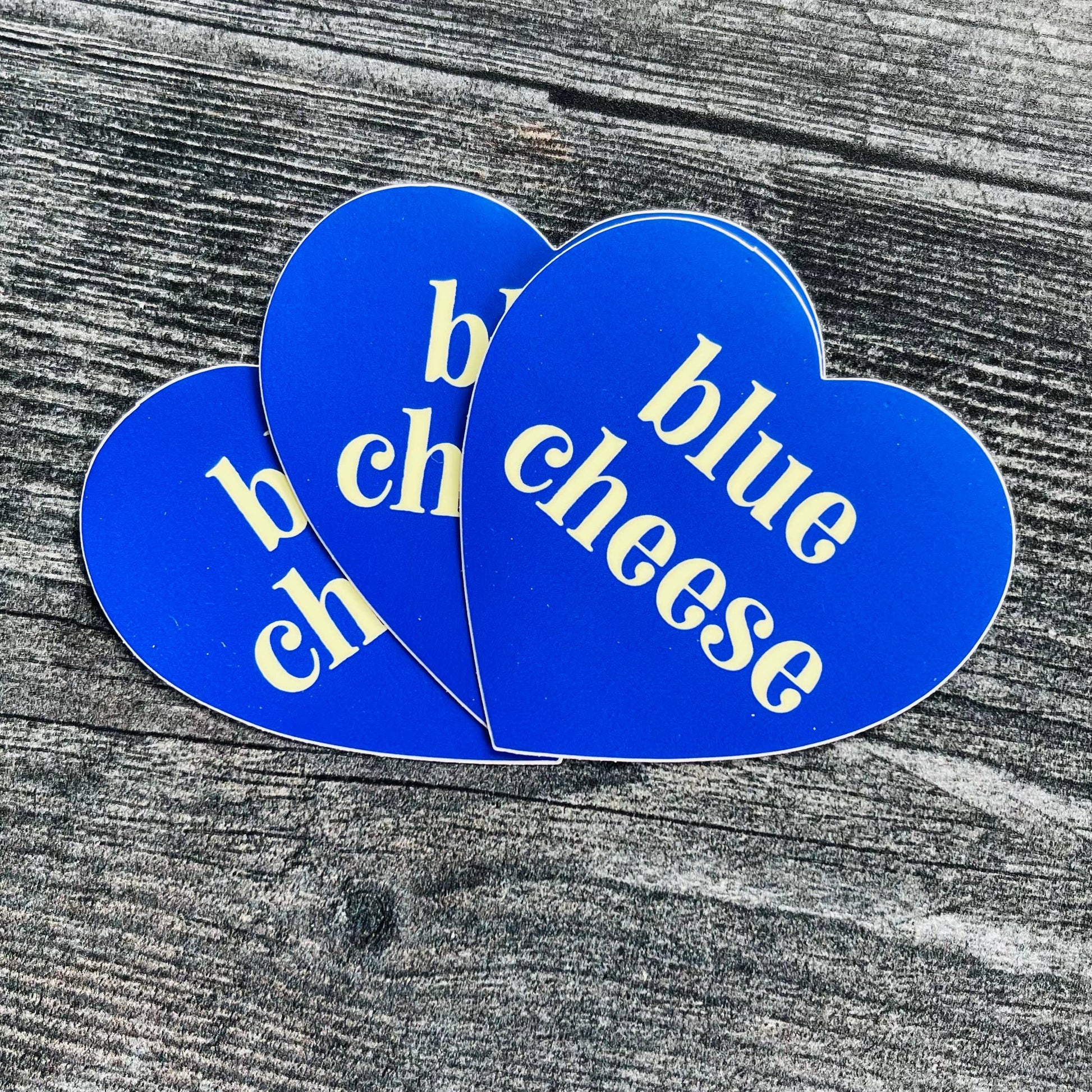 Three, blue, heart-shaped stickers with text in center that says "blue cheese"