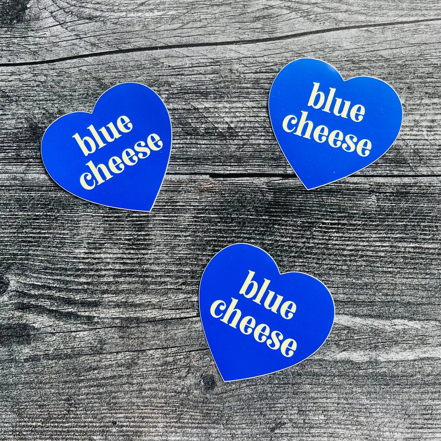 Three, blue, heart-shaped stickers with text in center that says "blue cheese"