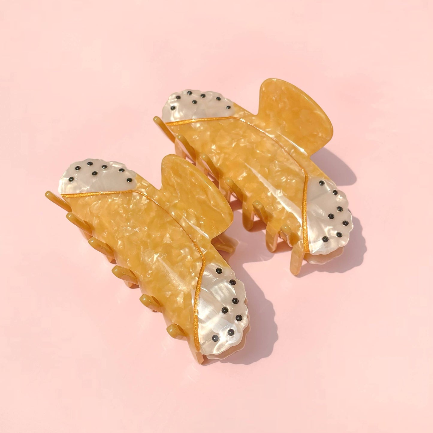 Pair of yellow cannoli-shaped hair clips on a pink background