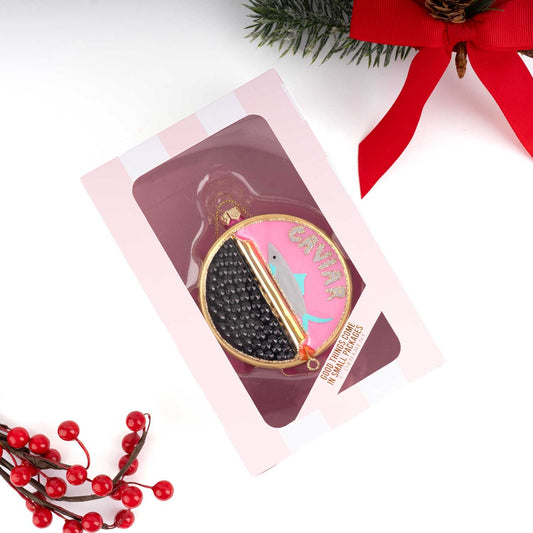 Decorative caviar tin ornament with a fish design in a pink box, surrounded by Christmas decorations.