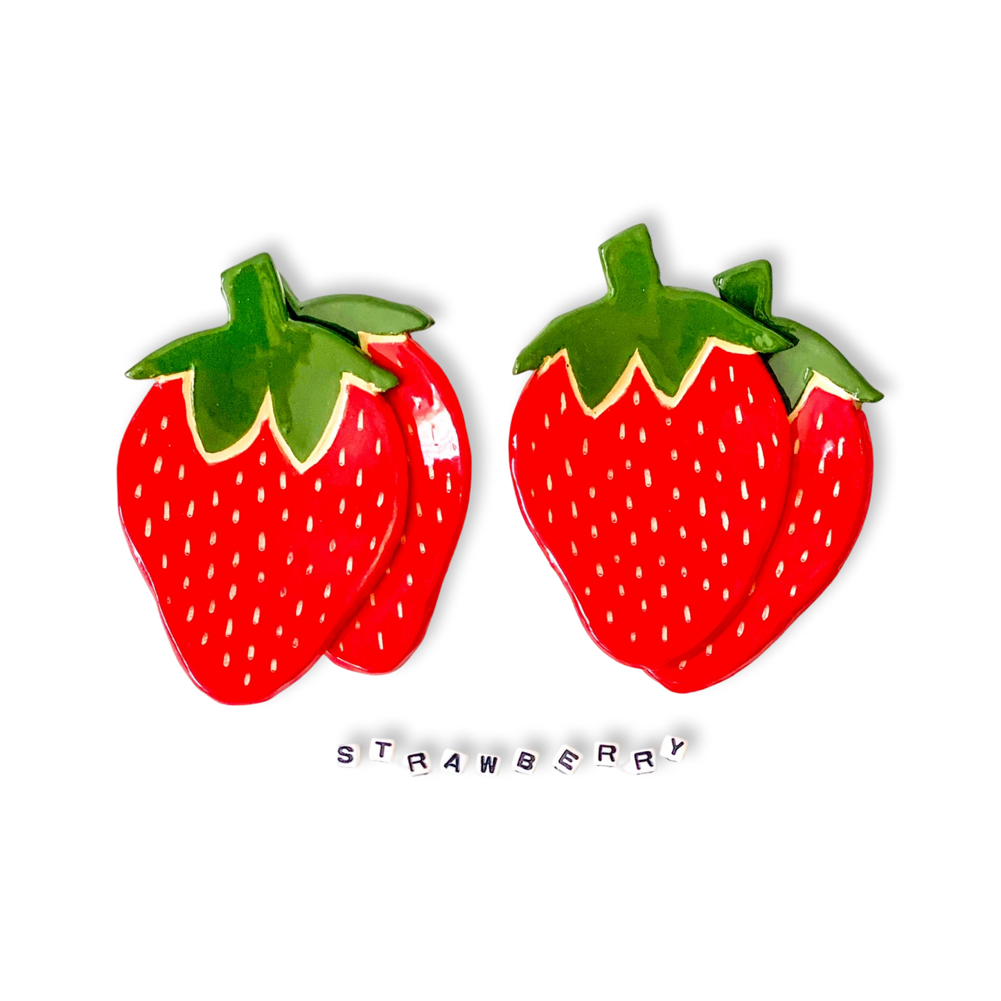 Two red strawberry trinket dishes with green leaves on a white background, accompanied by the word 'STRAWBERRY'.
