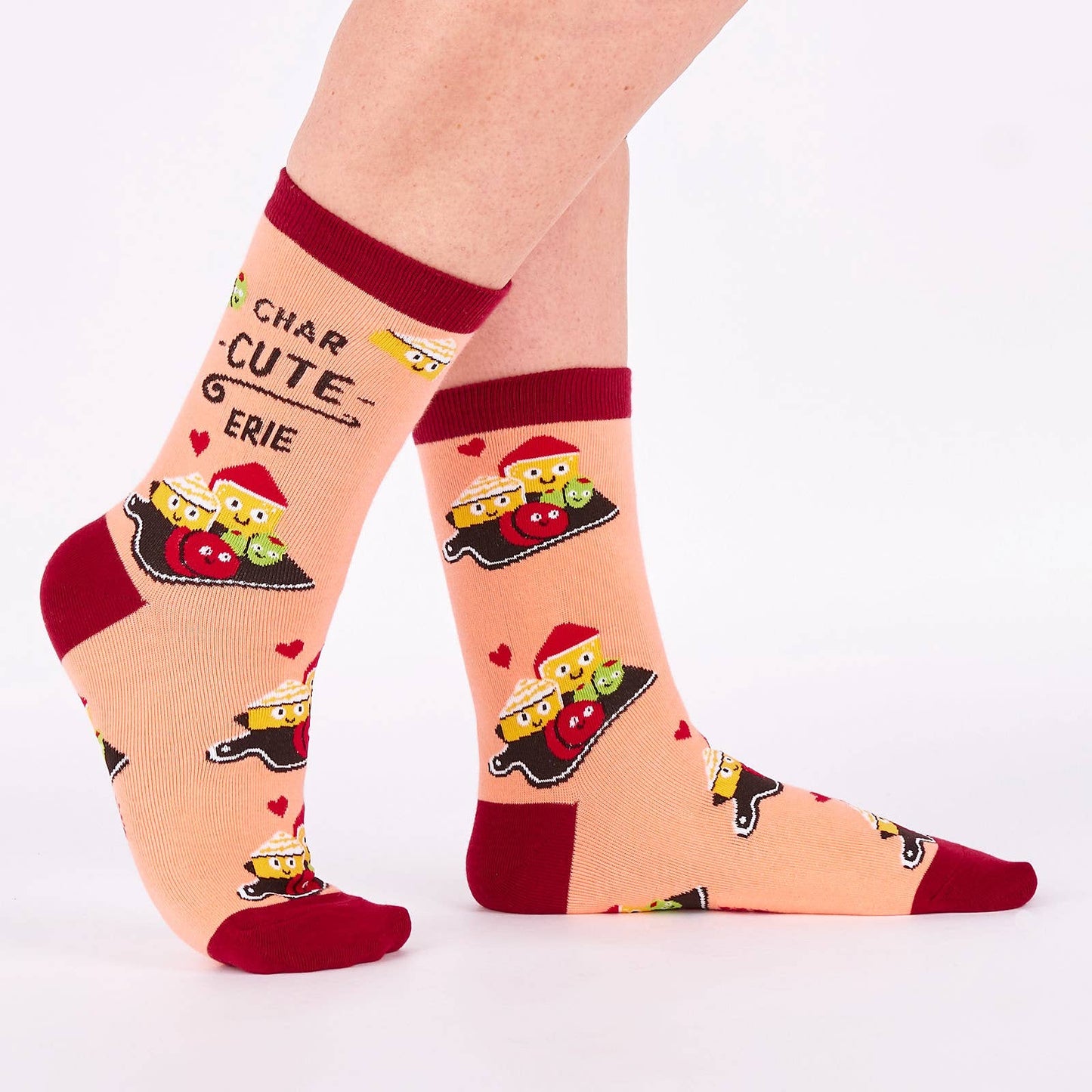 Pair of pink and burgundy socks with cartoon illustration of a charcuterie board design and text (char-CUTE-erie) on a white background