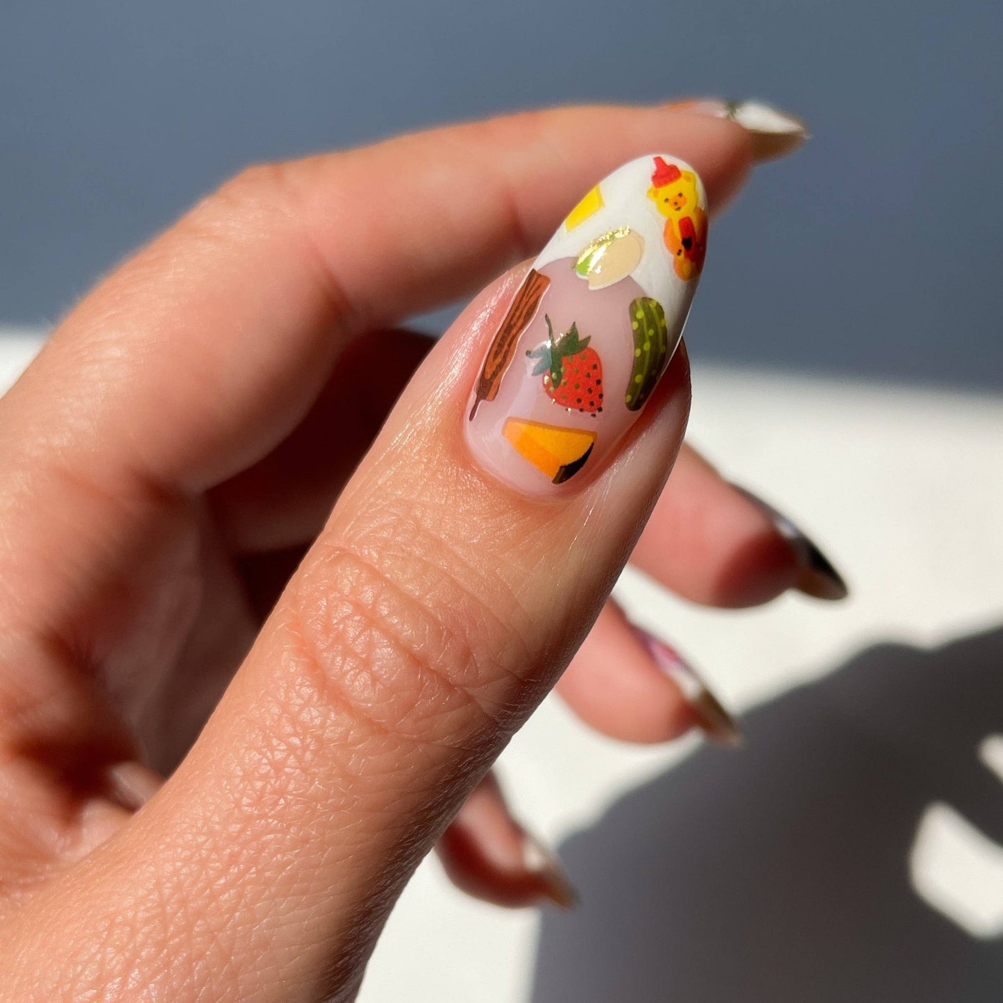 Nail with colorful design featuring fruits and vegetables on a neutral background