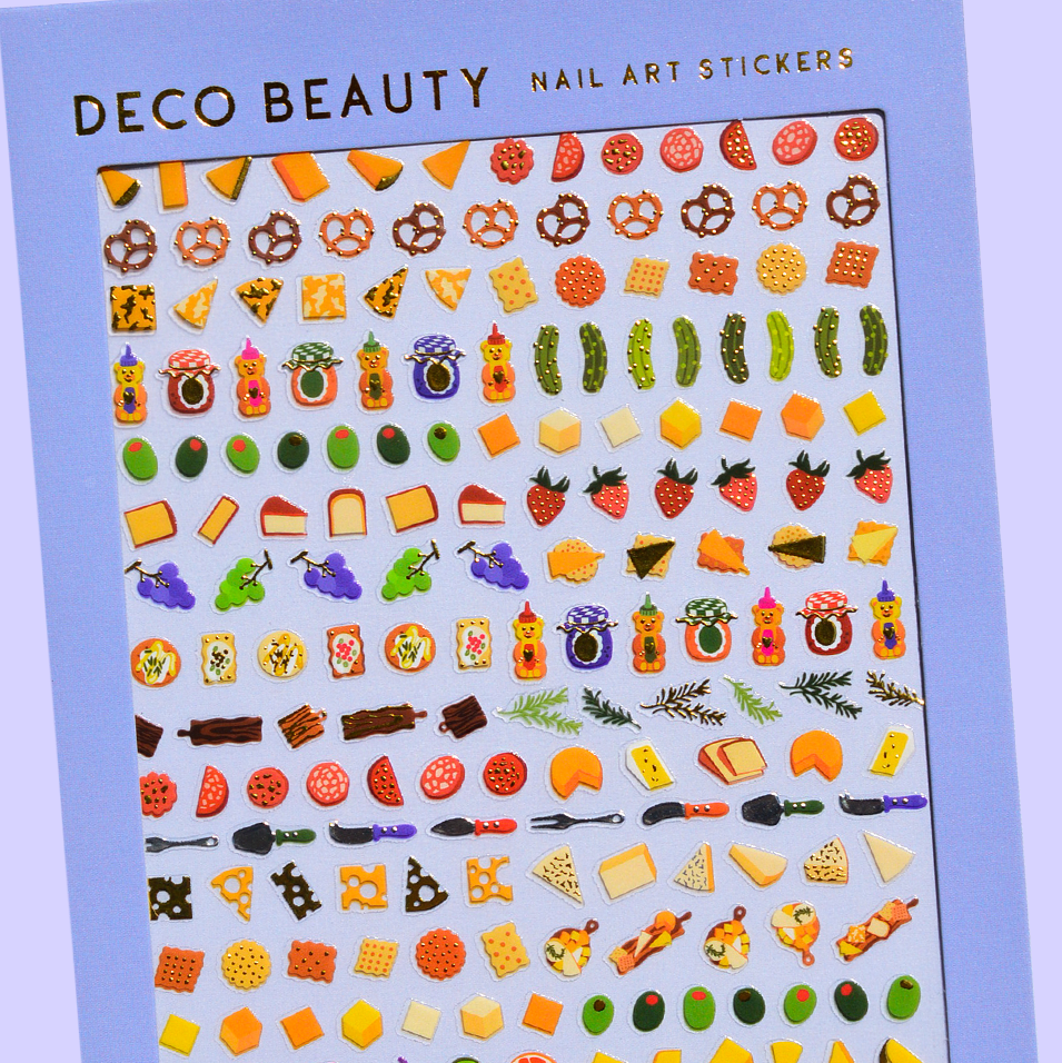 Sheet of Deco Beauty nail art stickers with various charcuterie-themed designs on a blue background.
