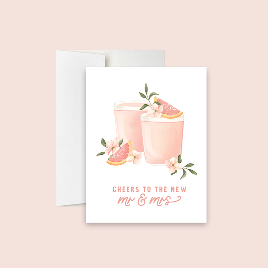 Greeting card with pink cocktails and grapefruit slices on a white background. Text reads "Cheers to the new Mr. & Mrs."