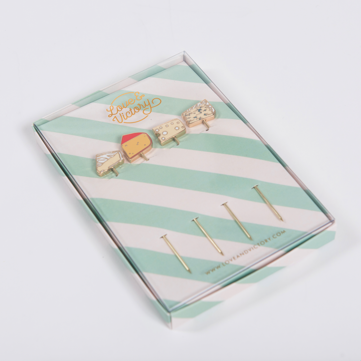Set of cheese-themed cocktail picks in a striped box with 'Love & Victory' branding on a light gray background
