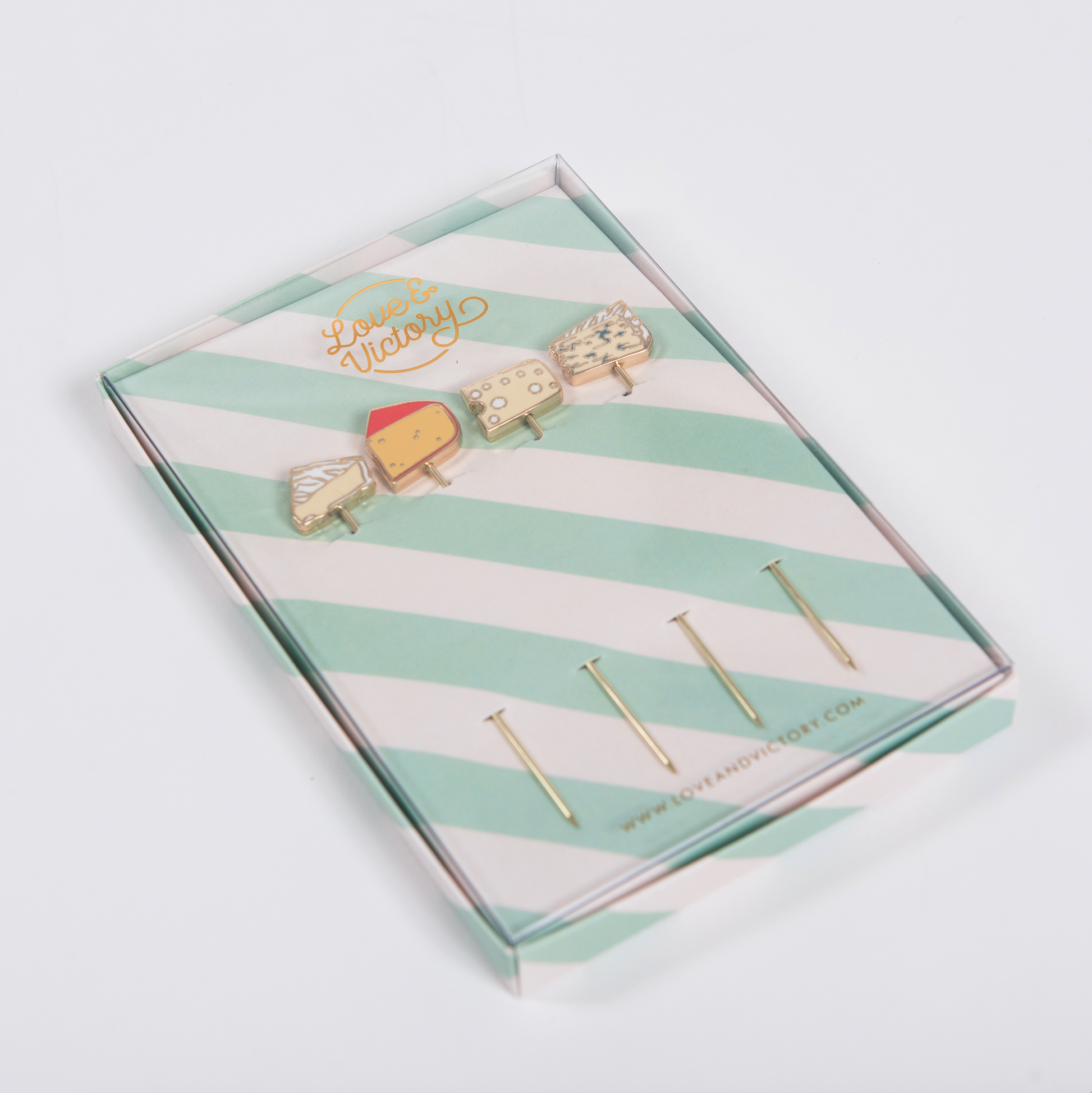 Set of cheese-themed cocktail picks in a striped box with 'Love & Victory' branding on a light gray background