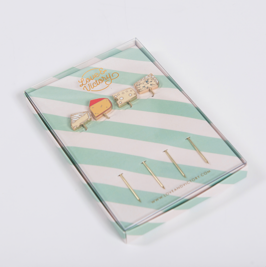 Set of cheese-themed cocktail picks in a striped box with 'Love & Victory' branding on a light gray background