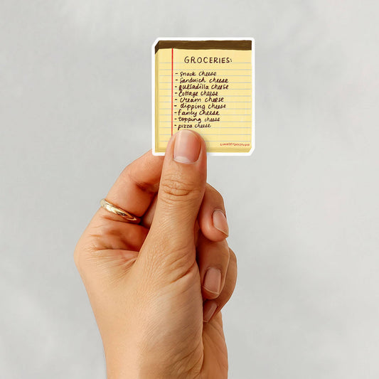 Hand holding a card with a cheese grocery list on a gray background