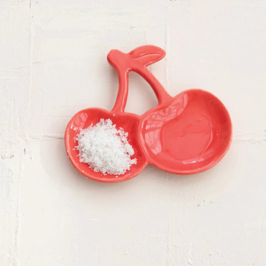 Red cherry-shaped trinket dish with salt inside on a white wooden surface