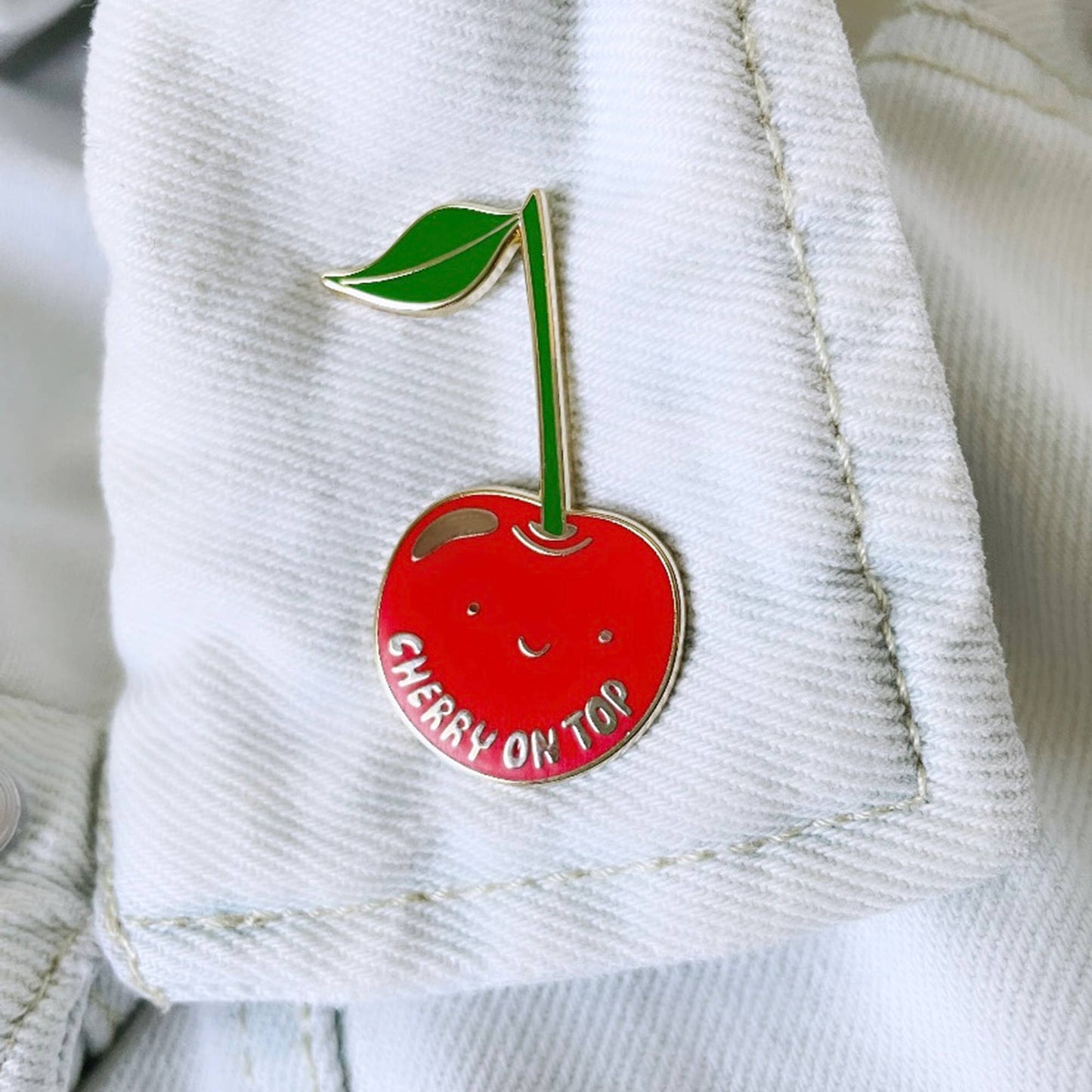 Cherry-themed enamel pin on a denim jacket