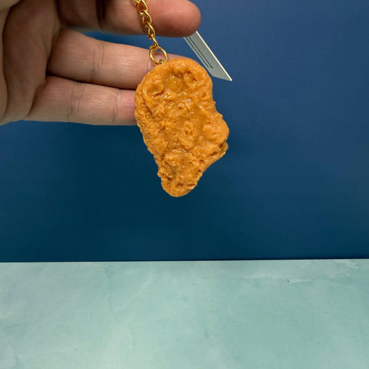 Hand holding a keychain shaped like a chicken nugget against a blue background