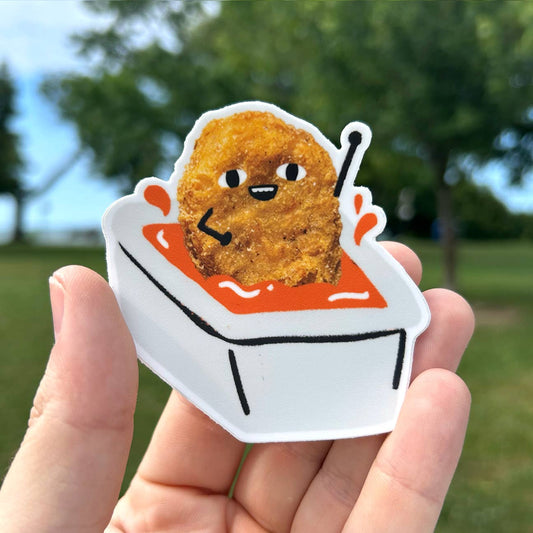 Sticker of a fried chicken nugget in sauce held by a hand with a blurred green outdoor background