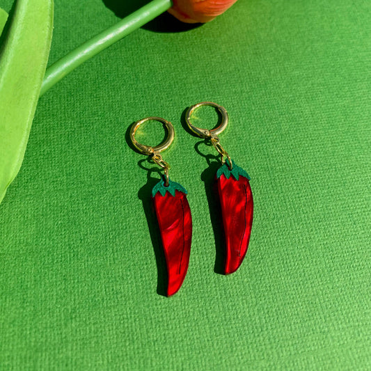 Red chili pepper earrings on a green background with a tulip.