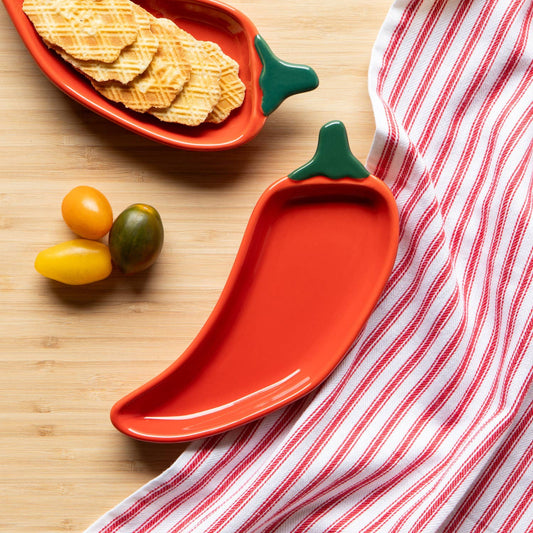 Red chili pepper-shaped dish with snacks on a wooden surface