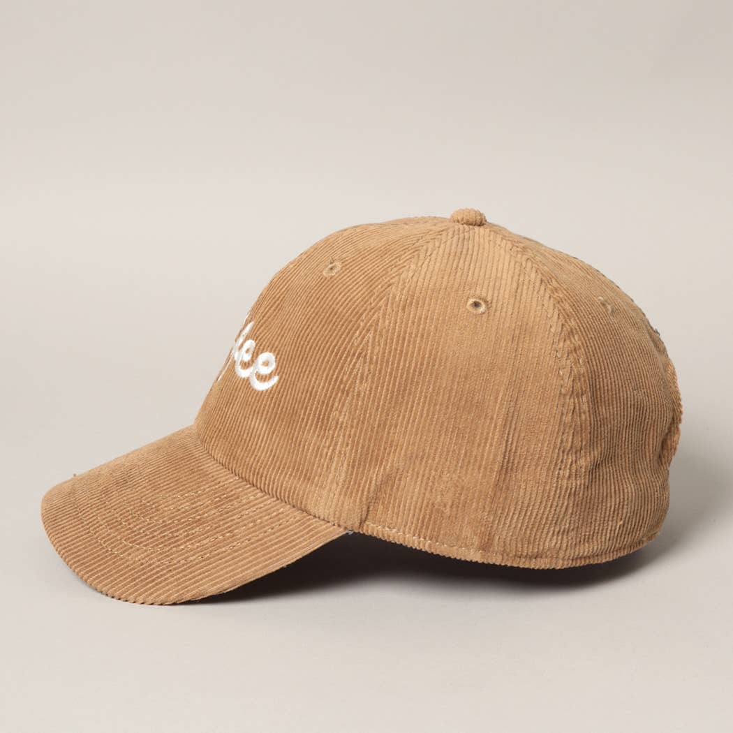 Side view of the tan/light brown corduroy baseball hat with white embroidered text that says "coffee"